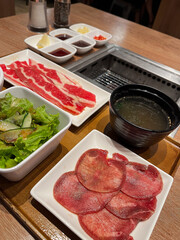 A beautifully arranged platter of sliced meat, salad, and condiments ready for grilling in a warm dining setting.