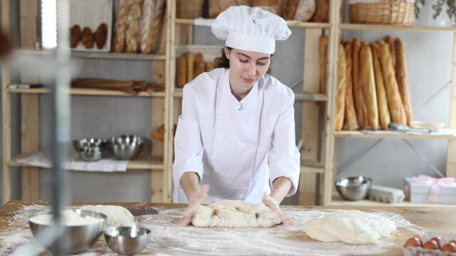 Girl works in bakery, kneads dough, works with flour. Working moment, process of creating croissants in bakery. She hardly knead tight dough, combine flour, water and other ingredients to make dough