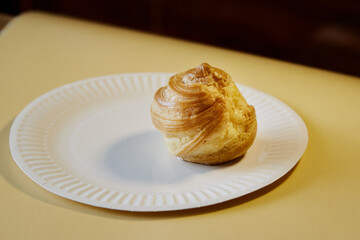 Bitten French pastry profiterole on a white plate against a light background, close-up texture of baking, close-up of cream pastries
