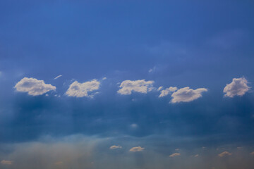 A line of small clouds in a dark blue sky in sunlight, close-up.