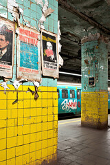 Obraz premium dimly lit underground station, vintage advertisement posters peeling from tiled walls, spray-painted subway car in background