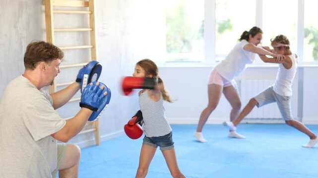 Girl and dad are boxing in gym, father helps daughter child to work out force of blow. Modern positive family chooses active hobby