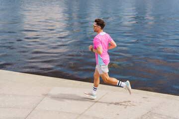 A Young Man Jogging in Bright Pink Attire Along the Riverside Pathway on a Sunny Day