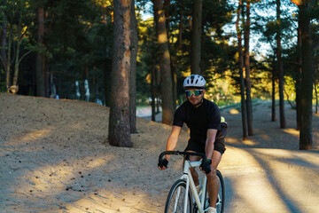 Fototapeta premium A Cyclist Navigates a Sandy Trail Surrounded by Tall Trees During Late Afternoon Light