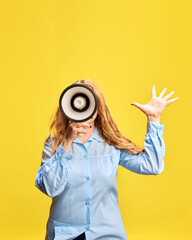 Fototapeta premium Young woman in blue shirt with megaphone against yellow studio background. Seasonal sale Announcement, promotion of weekly specials. Concept of sales, shopping, news, advertisement