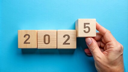 A hand placing wooden blocks with numbers to form 2025, symbolizing the transition to a new year and new beginnings. Perfect for concepts of change, progress and future goals.