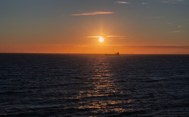 Transport ship and wind farm in the North Sea, sunset at Scheveningen, The Hague, Netherlands. NAtur, warm light, panorama, tranquil scene, clear sky.