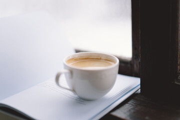 Cozy winter day with steaming coffee, open book, and candlelight by the snowy window