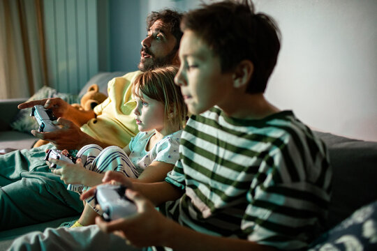 Father and children playing video games together on couch