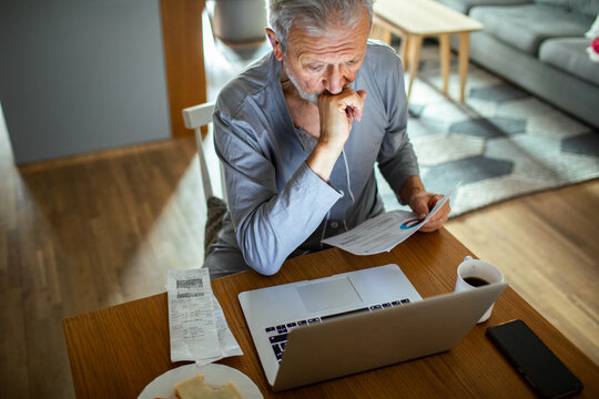 Elderly man reviewing bills and finances on laptop at home