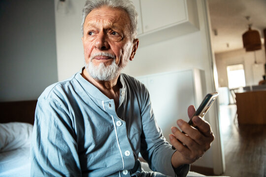 Elderly man in pajamas holding phone and looking concerned
