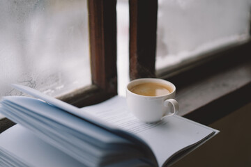 Cozy winter day with steaming coffee, open book, and candlelight by the snowy window