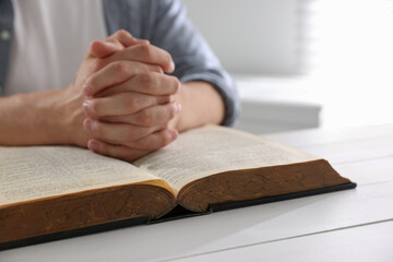 Man with Bible praying at white wooden table, closeup