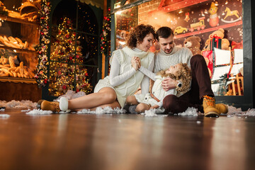 Young parents having fun with a cute little girl against the backdrop of Christmas trees, decorating with ornaments and decorating for the winter holiday season