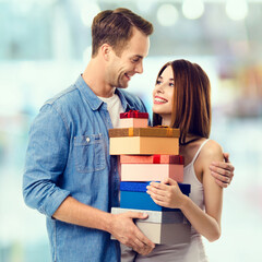 Happy smile couple with gift boxes. Holiday sales shopping, rebates, consumer credit ad concept. Man and surprised beautiful woman, boyfriend and girlfriend  blurred interior or mall store background.