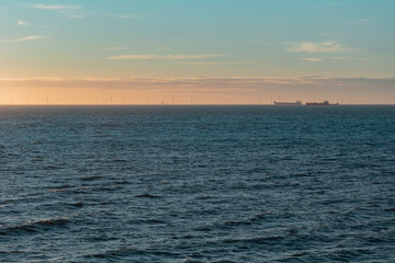 Fototapeta premium Silhouette of the wind farm at the horizon during twilight, two transport vessels on the right. Landscape at the Norht Sea, The Hague, Netherlands.