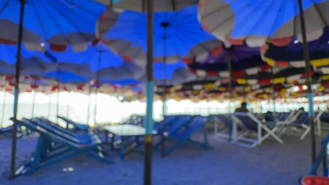 30 September 2024 Bang Saen Beach, Chonburi : A serene vista of a beachside cafe with rows of blue and white lounge chairs, shaded by colorful umbrellas. The gentle blur captures the tranquil ambience
