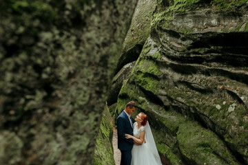 A couple is standing in a cave with moss growing on the walls. They are dressed in formal attire and appear to be happy