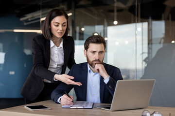 Two business professionals engaged in focused discussion using laptop and tablet in modern office....