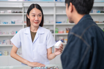 Asian professional female pharmacist using a digital tablet computer to dispense prescription medication to male customers. The doctor advises and explains to the client about the medication.