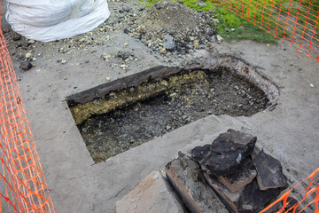 A hole in the asphalt with pieces of asphalt and dirt around it. The hole is surrounded by orange fencing