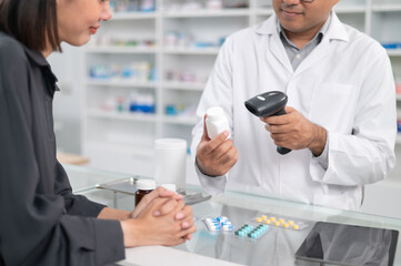 Asian professional male pharmacist using a tablet to dispense prescription medicines to female customers. The doctor advises and explains to the client how to use the medication.
