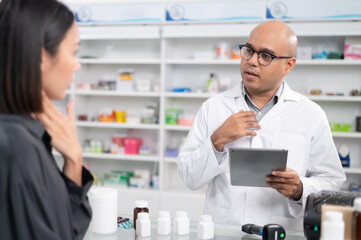 Asian professional male pharmacist using a tablet to dispense prescription medicines to female customers. The doctor advises and explains to the client how to use the medication.