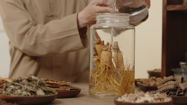 Video template with a close-up angle shows a scientist pouring water into a glass jar containing ginseng to begin the ginseng soaking process in a traditional medicine setting with natural ingredients