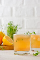 Homemade pear drink lemonade with lemon, rosemary, thyme and ice in a glasses on a light table. Healthy drink, sugar and alcohol free. Vertical orientation.