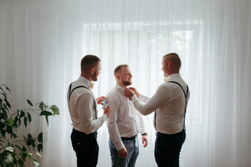 Fototapeta premium Three men are getting dressed up in front of a window