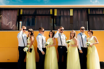 A group of men and women are posing for a photo in front of a yellow bus