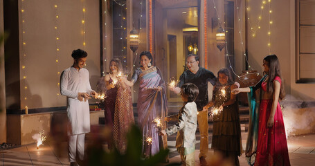 Indian Hindu Asian happy family teen girl boy child hold play crackers make fun joy night decor light diya home young adult male man female wife lady multi group older elder mom dad enjoy Diwali house