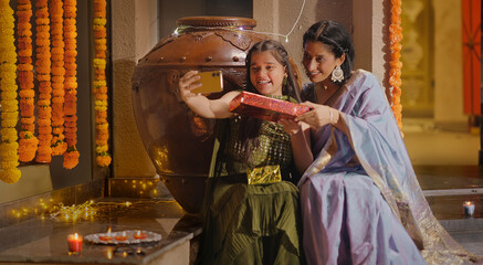 Indian Hindu happy mom cute girl child hold mobile use phone look cam take selfie photo pose decor diya light young adult mother child give gift vlog shoot video enjoy fun joy night spend time house