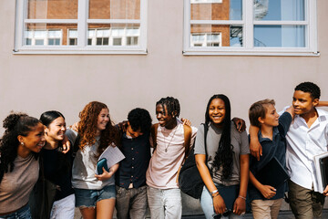 Multiracial male and female junior high students standing side by side near wall of school building