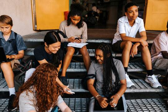 High angle view of male and female junior high students spending leisure time while sitting on steps in front of school