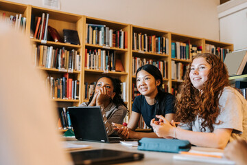 Female junior high students sitting with laptop in library at school