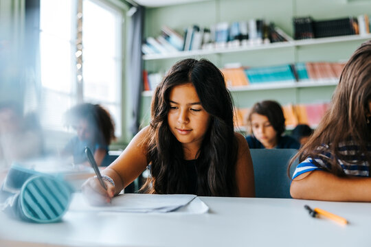 Focused schoolgirl with long hair giving exam while sitting in classroom at elementary school