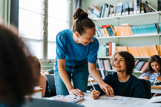 Smiling female professor helping elementary student with creativity in drawing class at school