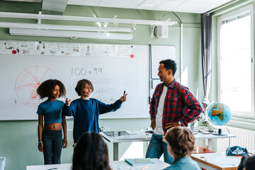 Professor with students explaining mathematics equations to pupils in classroom at school