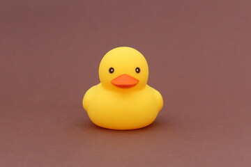A yellow rubber duck stands on a brown background.