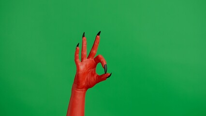 Creepy halloween devil monster hand in red paint with black nails shows ok good finger sign, isolated on chroma key green screen background, workspace mockup. © kinomaster