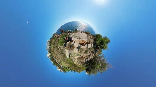 Tiny Planet effect of a Coastal Landscape, with a Man and Woman walking along a Cliffside Trail overlooking the Ocean, creating a spherical view of the scene.