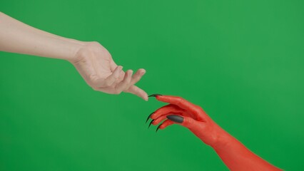 Creepy halloween devil monster hand in red paint with black nails touches fingers with female, isolated on chroma key green screen background, workspace mockup.