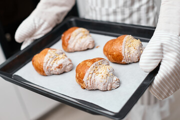 female baker holding metal tray with freshly baked crispy golden croissants