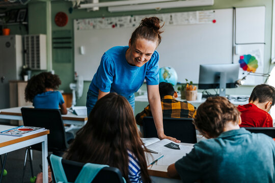 Happy female professor bending while talking with pupil in classroom at elementary school - Powered by Adobe