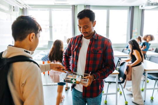 Male professor collecting smart phones of students while standing in classroom at elementary school