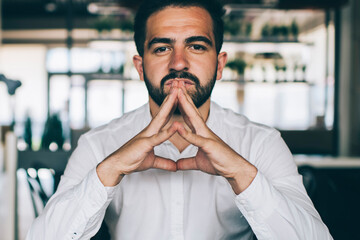 Portrait of serious Caucasian male entrepreneur in white shirt looking at camera while thinking on...