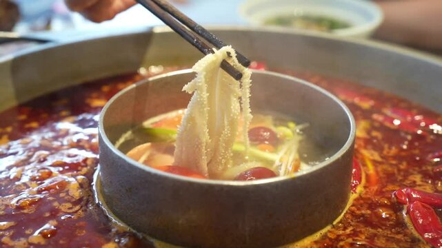 Close up slow motion of people having hotpot typical spicy Sichuan food at Chengdu China people using chopstick picking food from hot boiling soup.