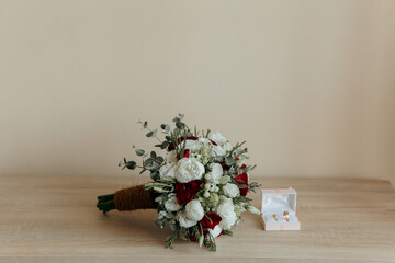A bouquet of red and white flowers sits on a table next to a white box with two gold earrings. The...