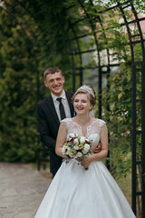 A bride and groom are posing for a picture in front of a green archway